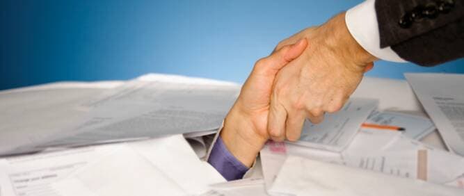 A handshake above a desk covered with financial paperwork.